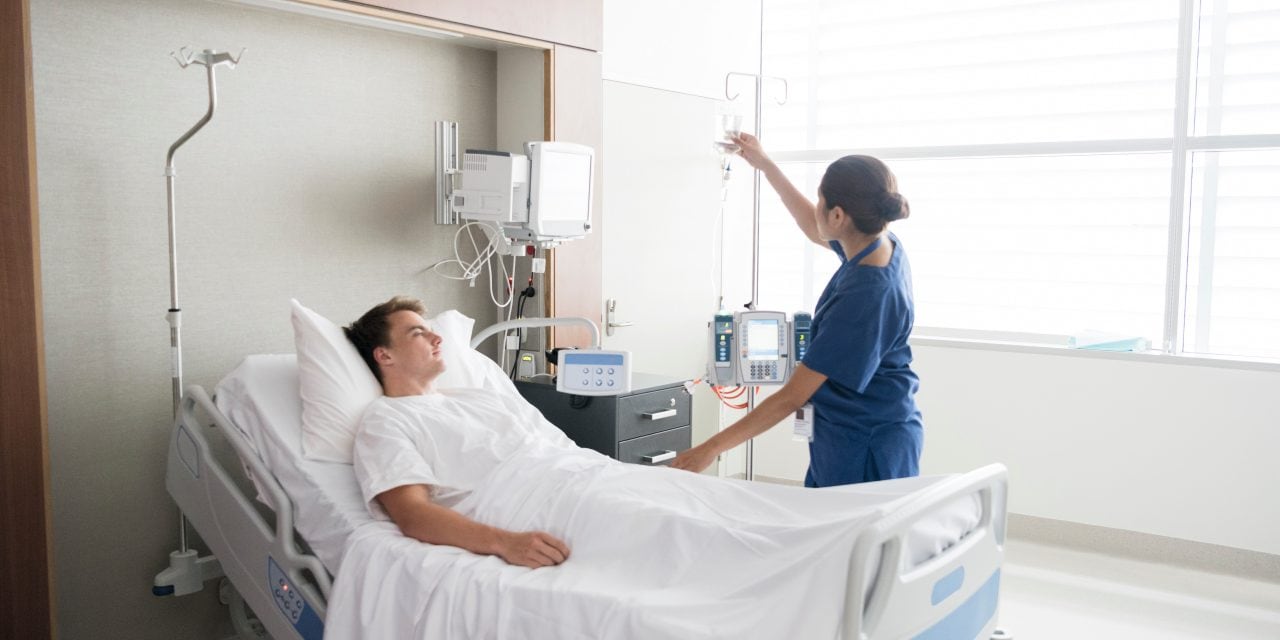 Young man in hospital being cared for by nurse. Medical professional looking after patient on hospital ward. Adjusting iv line, medication, care, bedside manner.